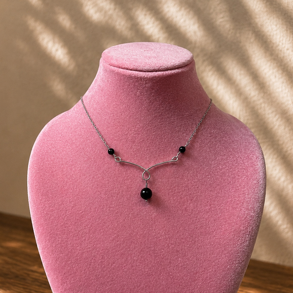 Necklace with black beads on a pink velvet stand against a beige wall.