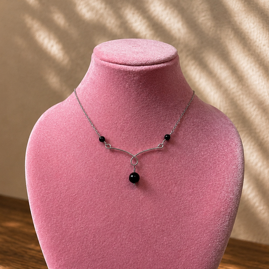 Necklace with black beads on a pink velvet stand against a beige wall.