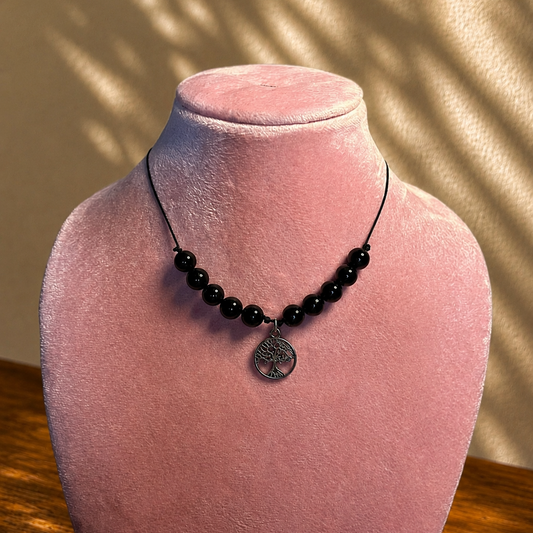 Black beaded necklace with a pendant on a pink velvet mannequin bust.