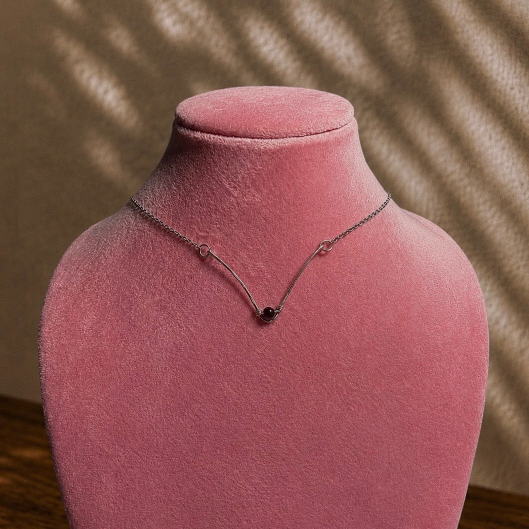 Necklace with a black pendant on a pink velvet mannequin bust against a neutral background