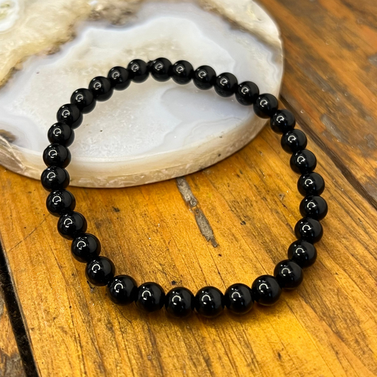 Black beaded bracelet on a wooden surface with a stone background
