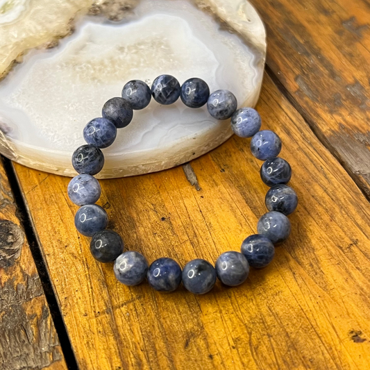 Blue beaded bracelet on a wooden surface with a shell in the background