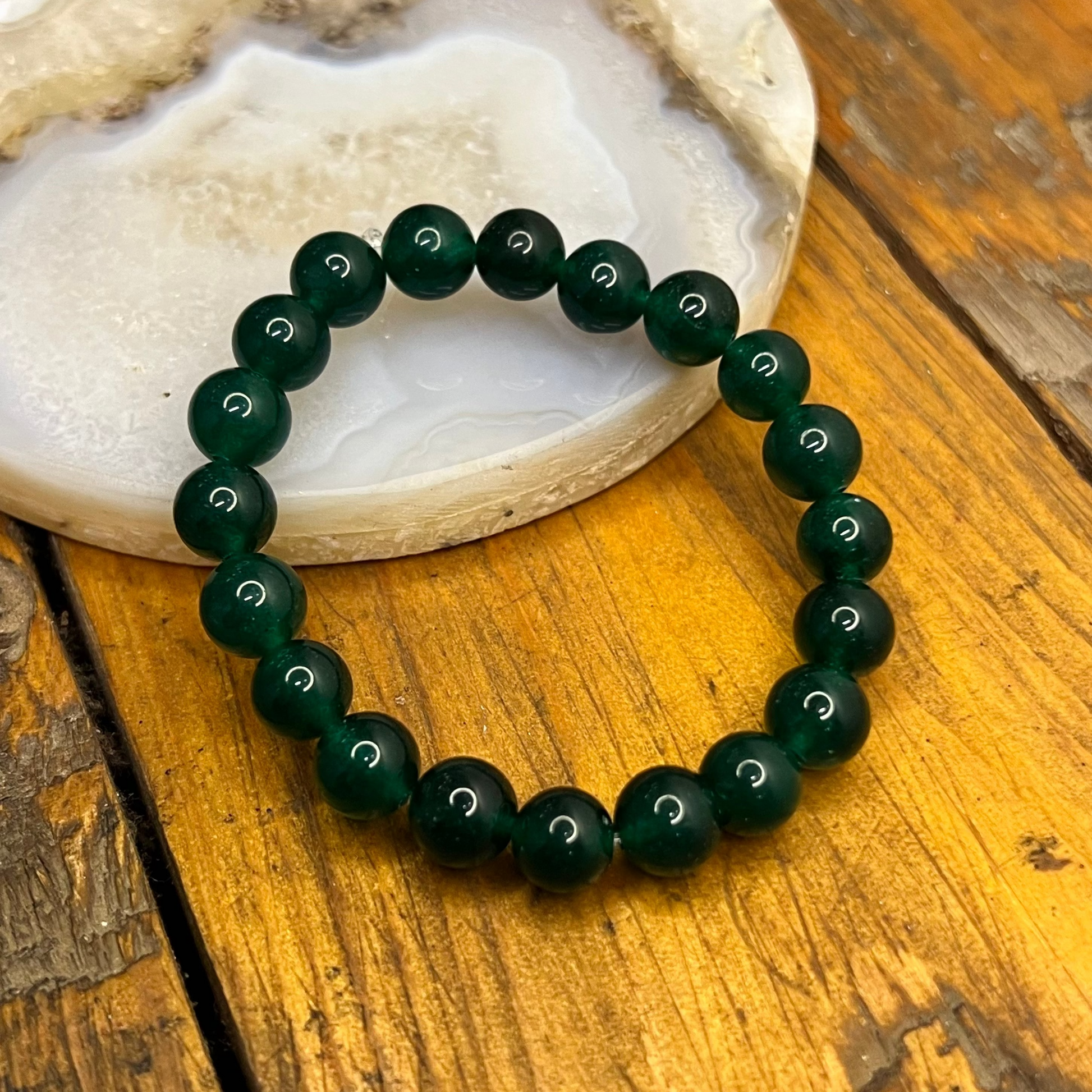 Green beaded bracelet on a wooden surface with a stone background
