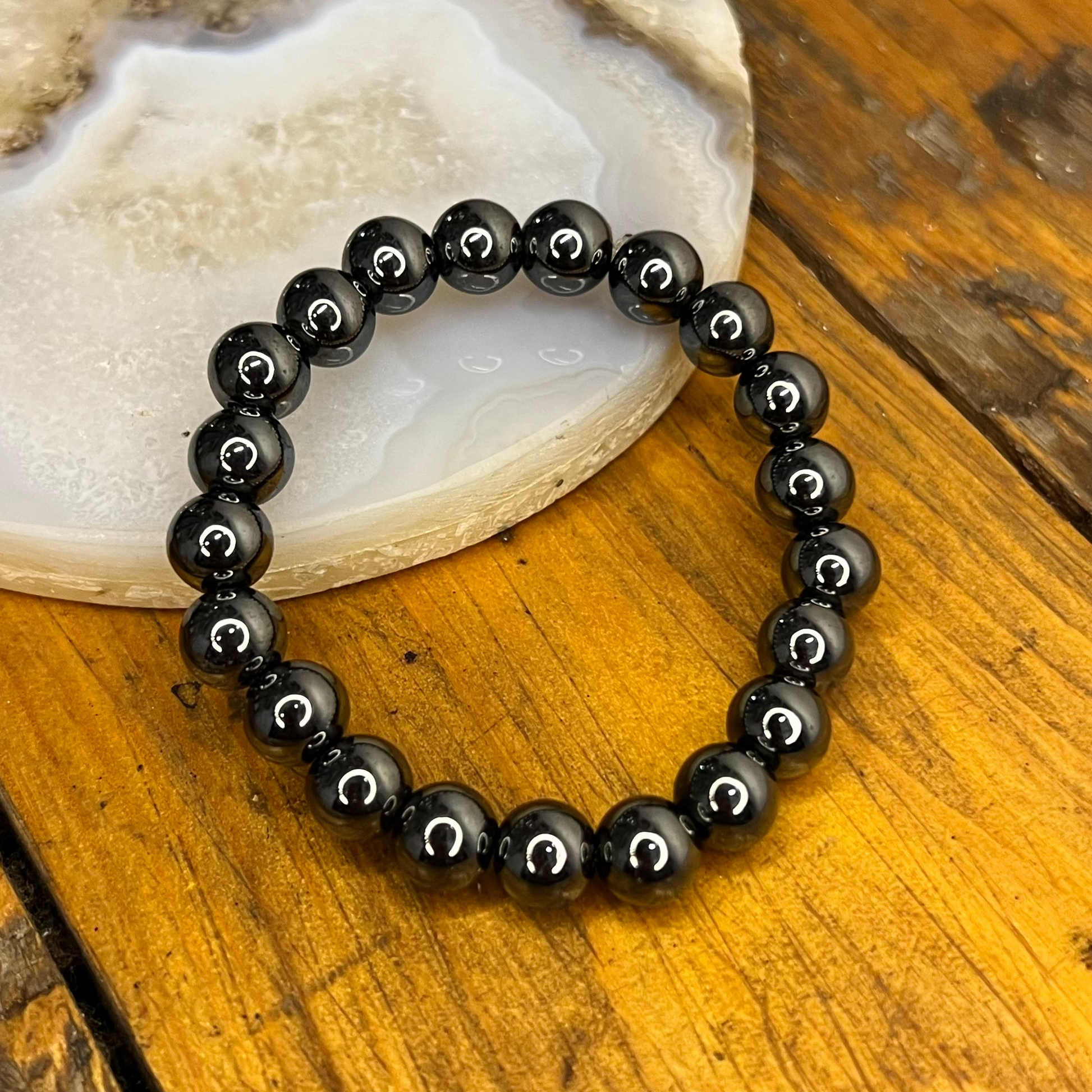 Black beaded bracelet on a wooden surface with a stone background