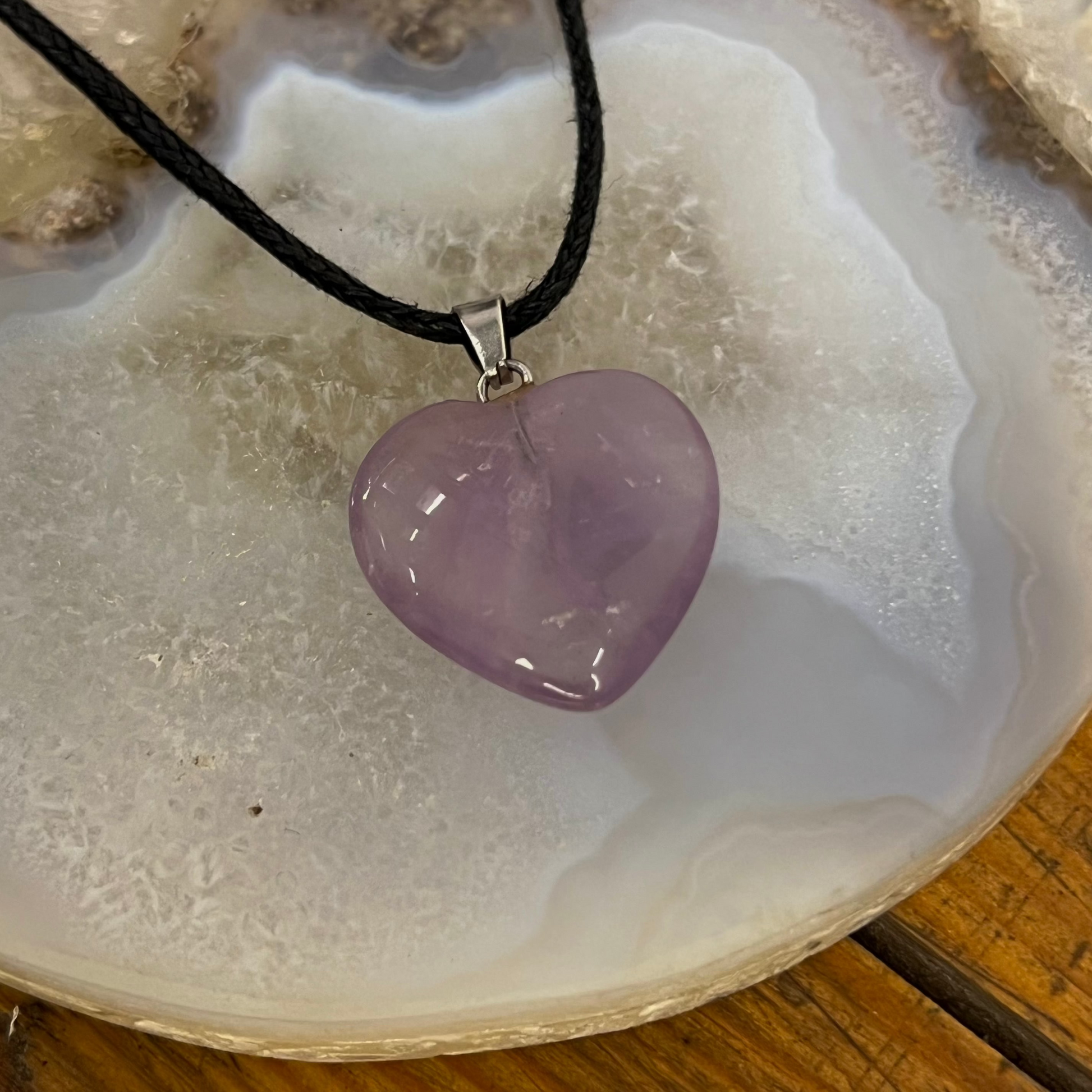 Purple heart-shaped pendant on a black cord over a white stone surface