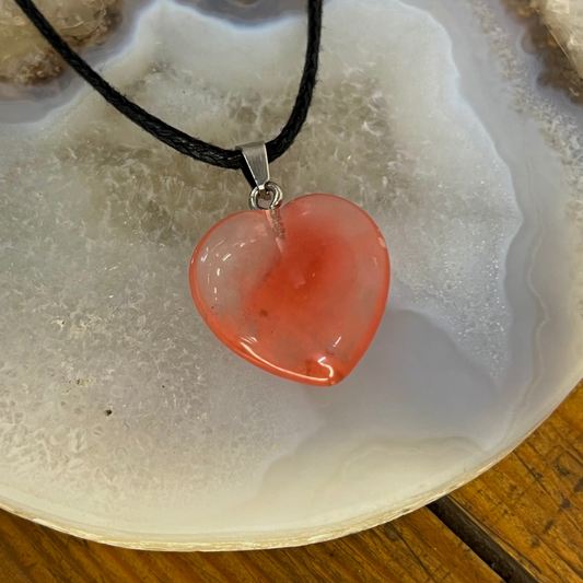 Heart-shaped pendant on a black cord against a textured stone background